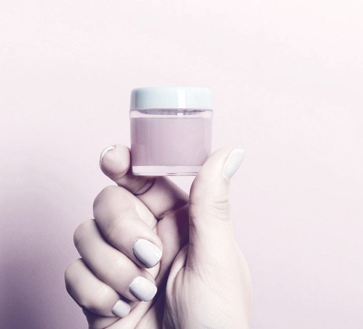 A hand holding a small jar of cream